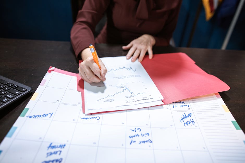 Person writing on a financial document on an organized desk with a calendar.